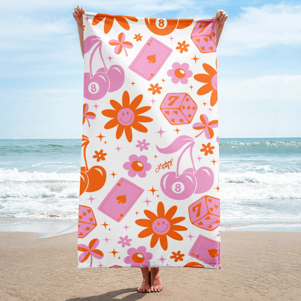 Retro beach towel with hand-illustrated pattern of cherries, smiley flowers, lucky dice, hearts, and stars, perfect for summer. In pink and orange.