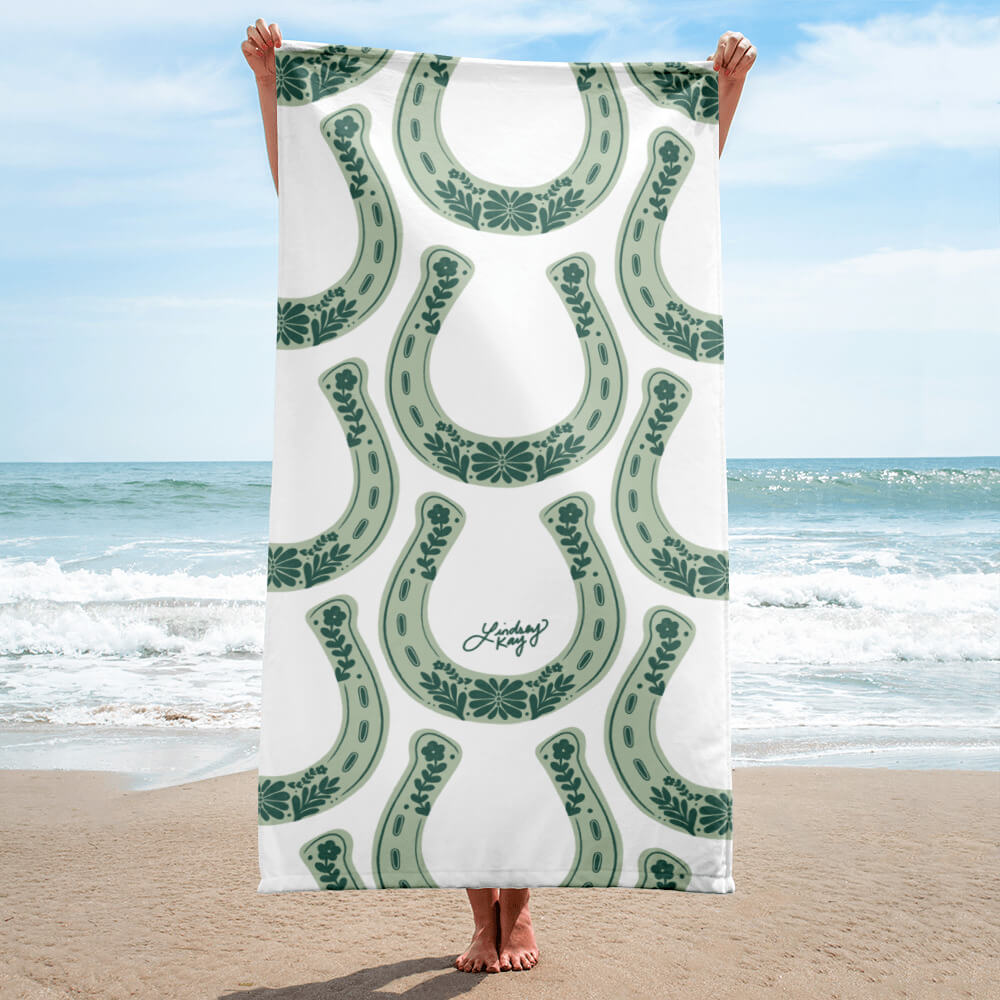 Hand illustrated western beach towel by Lindsey Kay Collective. Features bold western-inspired design, sized 30×60 inches. Made of soft polyester-cotton blend with absorbent white terry cloth backing. Perfect for beach days, poolside, or summer gifts for cowgirls.