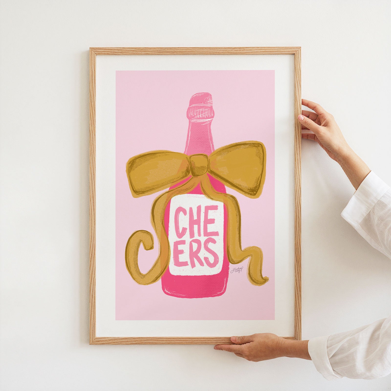 Hand drawn pink champagne bottle art print with gold ribbon that says 'Cheers.' Designed by Lindsey Kay Collective. Perfect for bar cart décor, kitchen walls, or celebratory gallery spaces. Printed on enhanced matte paper, available in multiple sizes.